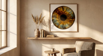 A sunlit minimalist living room featuring a large circular framed artwork with organic iris-like patterns in amber and teal tones, styled with ceramics and dried botanicals on a warm plaster wall.