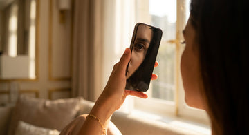 A person holding a smartphone close to their eye in soft natural light, with a warm, blurred background evoking intimate iris photography at home.